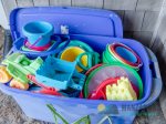 A bucket of beach toys is located under the front stairs outside.